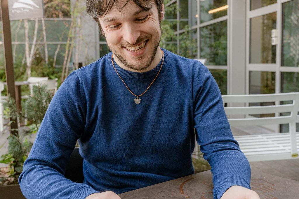 Davide riccio lancia dei dadi da dungeons and dragons. indossa una felpa blu. sullo sfonod un locale verde