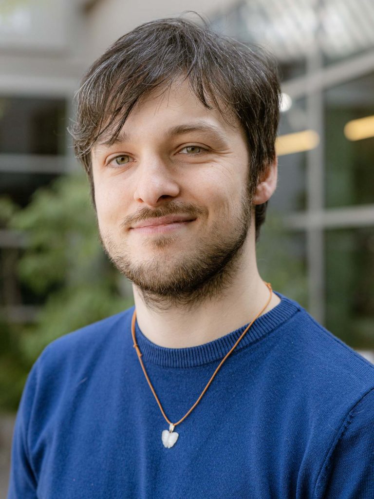 davide riccio, guarda l'osservatore con una maglia azzurra e un ciondolo bianco