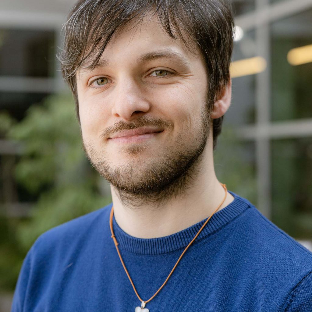 davide riccio, guarda l'osservatore con una maglia azzurra e un ciondolo bianco